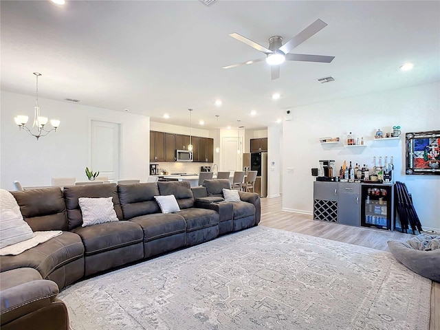 living room featuring ceiling fan with notable chandelier, bar area, beverage cooler, and light hardwood / wood-style flooring