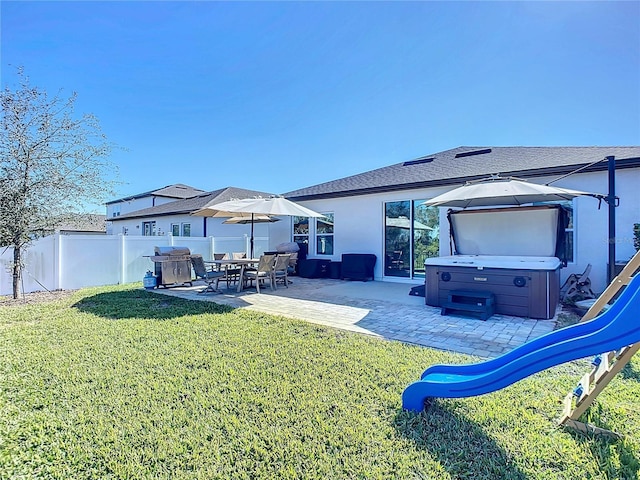 back of property with a yard, a patio area, and a hot tub