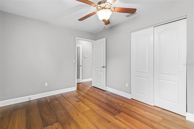 unfurnished bedroom with ceiling fan, a closet, hardwood / wood-style floors, and a textured ceiling