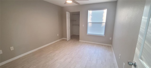 unfurnished bedroom featuring ceiling fan, a walk in closet, light wood-type flooring, and a closet