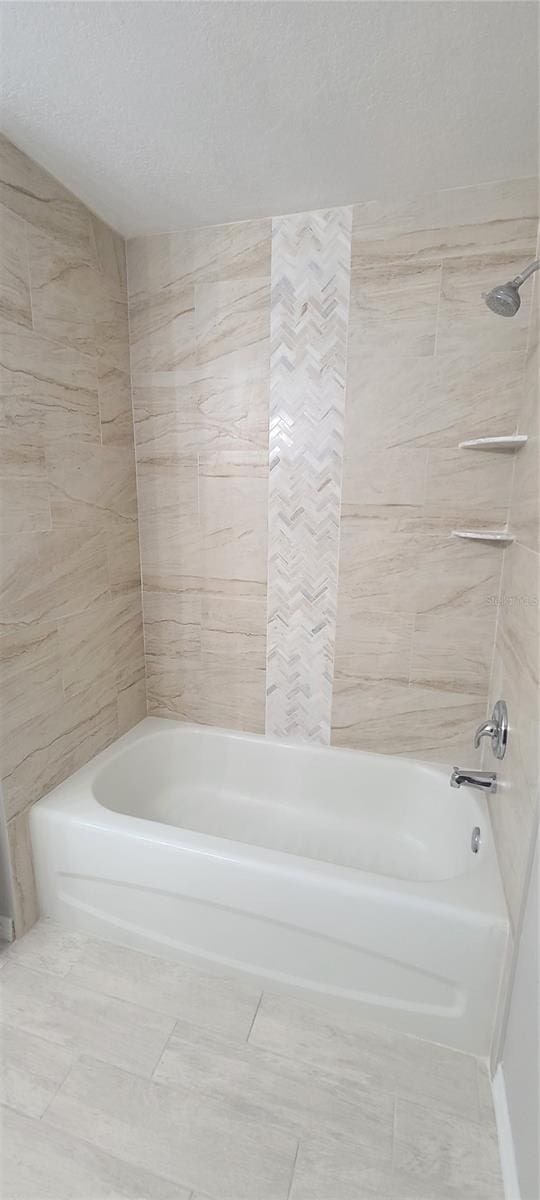 bathroom with tiled shower / bath combo and a textured ceiling