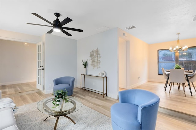 living room featuring ceiling fan with notable chandelier and light wood-type flooring