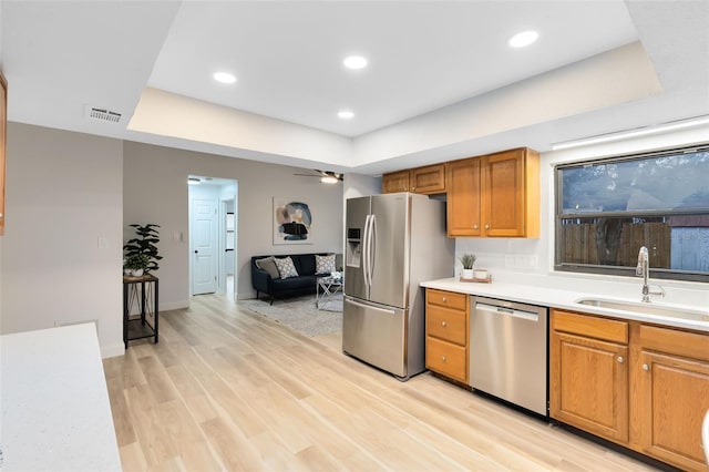 kitchen with appliances with stainless steel finishes, light hardwood / wood-style floors, sink, a raised ceiling, and ceiling fan