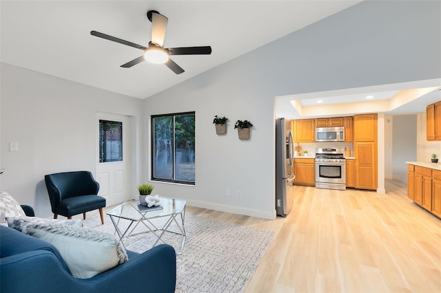 living room featuring ceiling fan, vaulted ceiling, a tray ceiling, and light hardwood / wood-style flooring