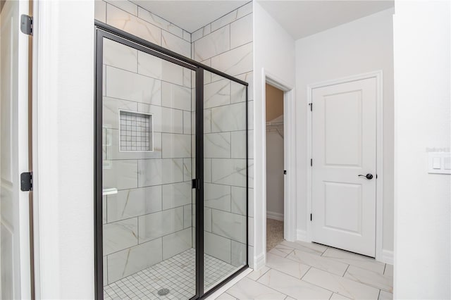 bathroom featuring marble finish floor, baseboards, a walk in closet, and a stall shower