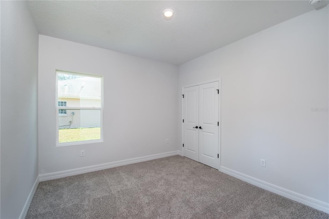 carpeted empty room featuring a textured ceiling and baseboards