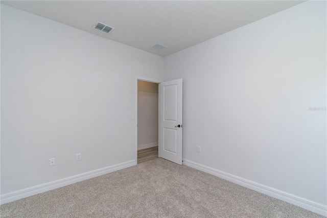 spare room featuring light carpet, visible vents, and baseboards