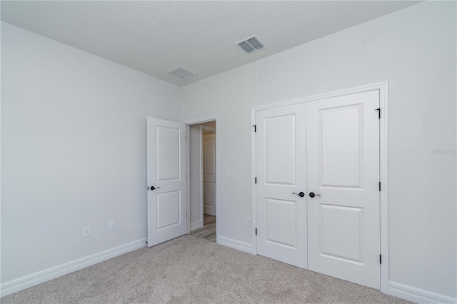 unfurnished bedroom featuring a textured ceiling, carpet flooring, visible vents, baseboards, and a closet