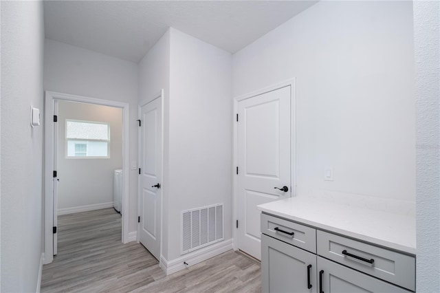 corridor featuring light wood finished floors, washer / dryer, visible vents, and baseboards