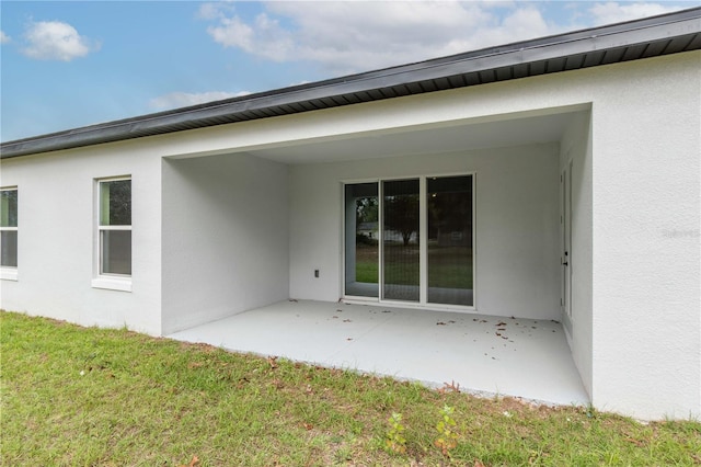 back of property featuring a patio, a lawn, and stucco siding