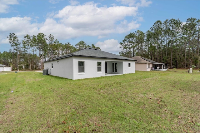 back of house featuring central AC unit, a lawn, and stucco siding