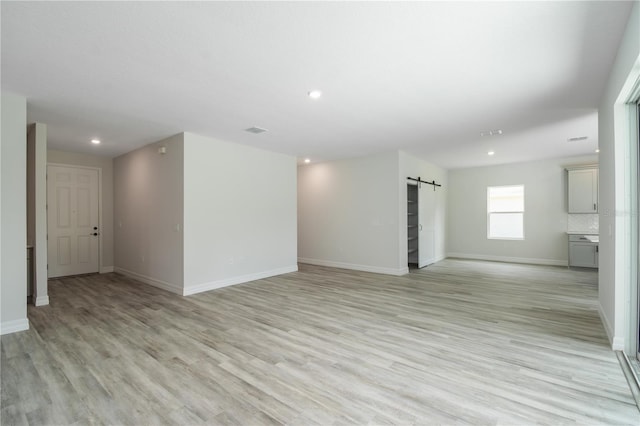 empty room featuring light wood-style floors, baseboards, and a barn door