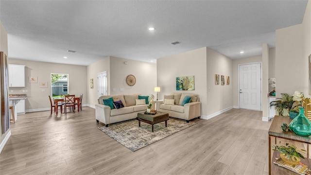 living room with baseboards, light wood-style flooring, visible vents, and a textured ceiling