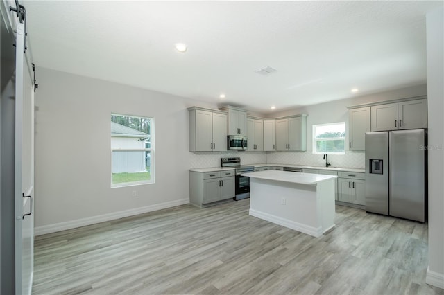 kitchen featuring a barn door, appliances with stainless steel finishes, decorative backsplash, and gray cabinetry