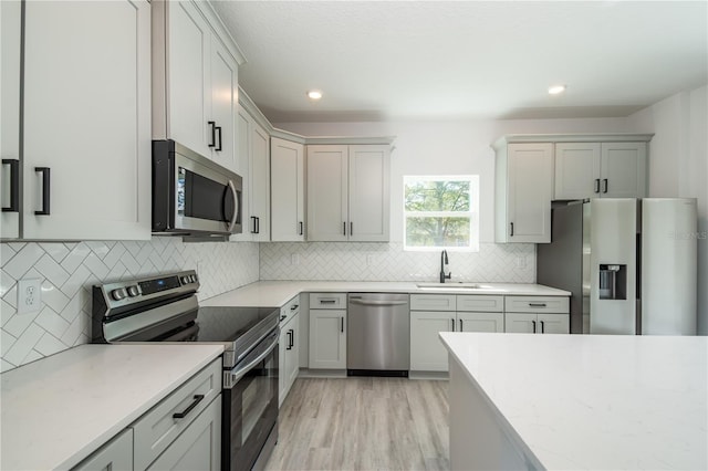 kitchen featuring decorative backsplash, stainless steel appliances, light wood-style floors, a sink, and recessed lighting