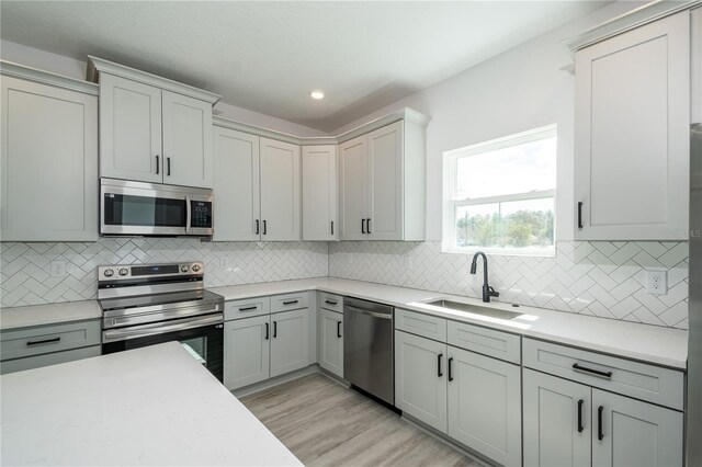 kitchen featuring recessed lighting, backsplash, light wood-style flooring, appliances with stainless steel finishes, and a sink