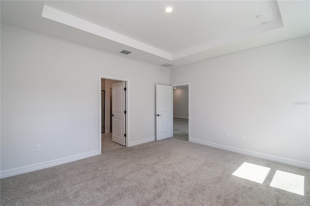 spare room with a tray ceiling, visible vents, light carpet, and baseboards