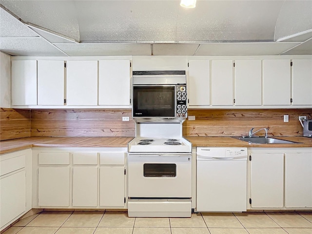 kitchen with white appliances, white cabinetry, light tile patterned flooring, and sink