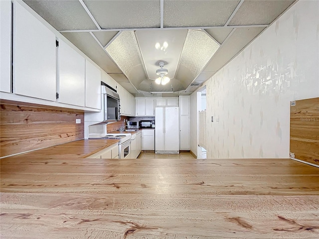 kitchen with white appliances, ceiling fan, white cabinetry, and kitchen peninsula