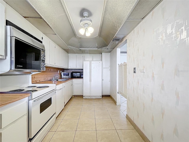 kitchen featuring white appliances, a raised ceiling, white cabinets, light tile patterned flooring, and sink