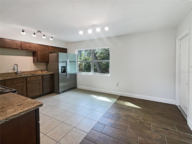 kitchen featuring dark stone countertops, stainless steel fridge, sink, and dark brown cabinets