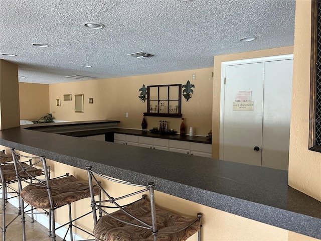 kitchen with a kitchen bar, kitchen peninsula, white cabinetry, and a textured ceiling