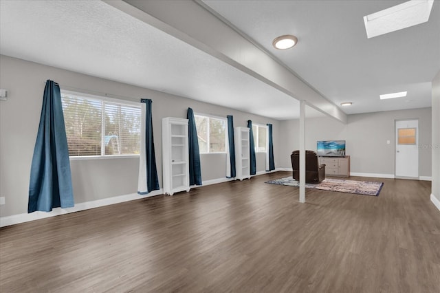 unfurnished living room featuring dark wood-type flooring, a skylight, and a textured ceiling