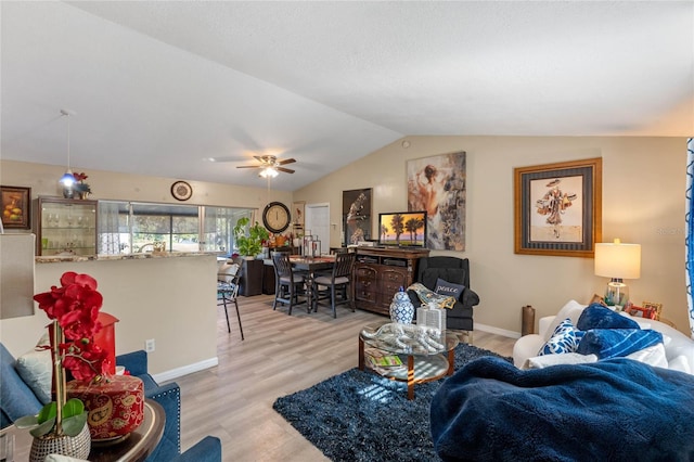 living room with ceiling fan, light hardwood / wood-style floors, and vaulted ceiling