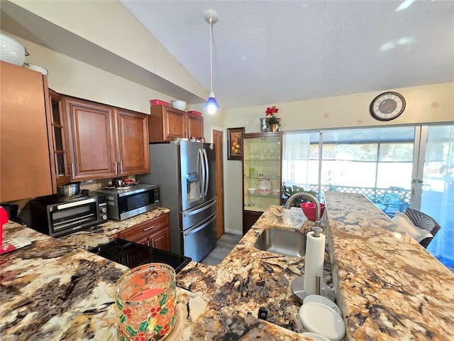 kitchen with light stone countertops, sink, pendant lighting, vaulted ceiling, and appliances with stainless steel finishes