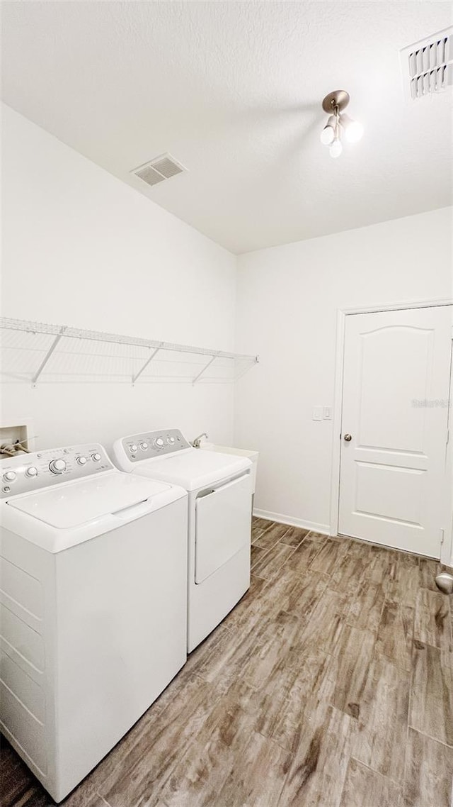 clothes washing area with washing machine and dryer, a textured ceiling, and hardwood / wood-style floors