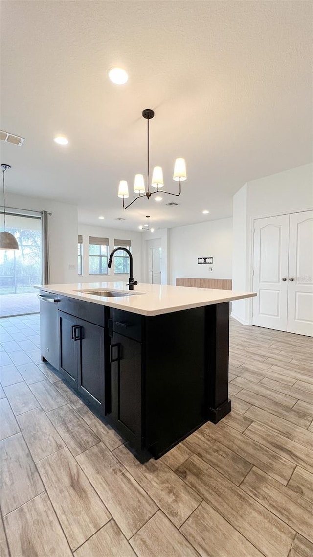 kitchen featuring hanging light fixtures, a kitchen island with sink, sink, and stainless steel dishwasher