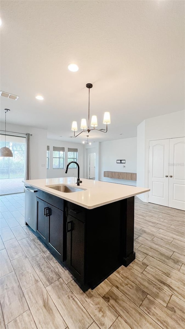 kitchen featuring sink, hanging light fixtures, stainless steel dishwasher, and a center island with sink