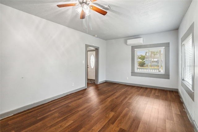 spare room with ceiling fan, a textured ceiling, a wall unit AC, dark wood-type flooring, and baseboards