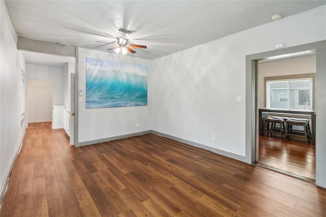 empty room with dark wood-style floors, baseboards, visible vents, and a ceiling fan