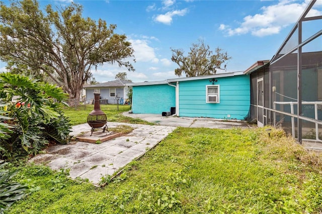 back of property featuring glass enclosure, a patio, a fire pit, fence, and a lawn