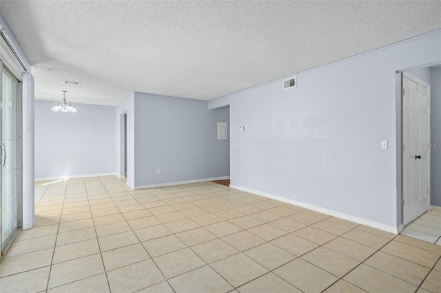 empty room featuring a chandelier, a textured ceiling, and light tile patterned flooring