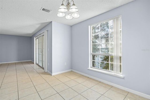 empty room with light tile patterned floors, a textured ceiling, and a notable chandelier