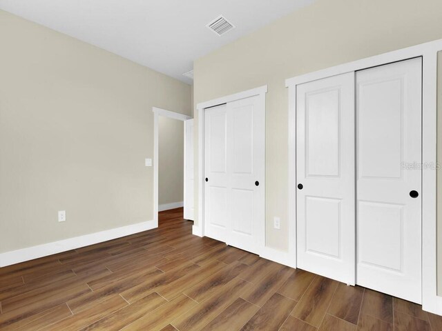 unfurnished bedroom with dark hardwood / wood-style flooring and two closets