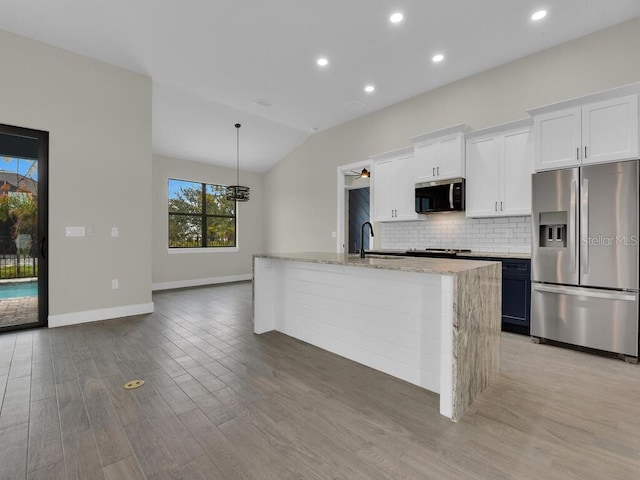 kitchen with a kitchen island with sink, light wood-style flooring, tasteful backsplash, appliances with stainless steel finishes, and light stone countertops