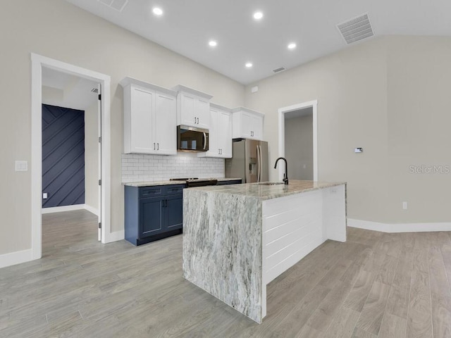 kitchen featuring light wood-type flooring, visible vents, an island with sink, a sink, and stainless steel appliances