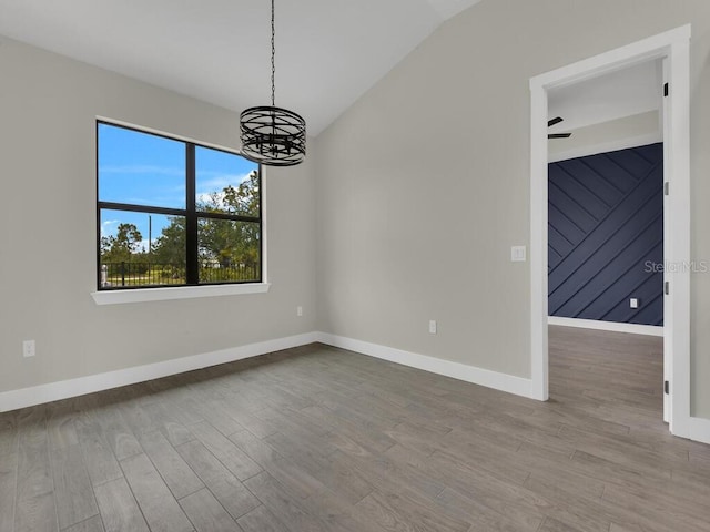 unfurnished room with vaulted ceiling, a notable chandelier, wood finished floors, and baseboards