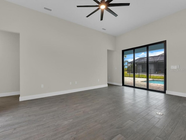 unfurnished room featuring dark wood-style floors, a ceiling fan, visible vents, and baseboards