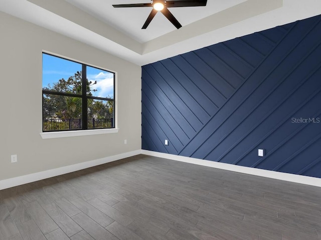 unfurnished room featuring baseboards, dark wood-type flooring, a raised ceiling, and ceiling fan