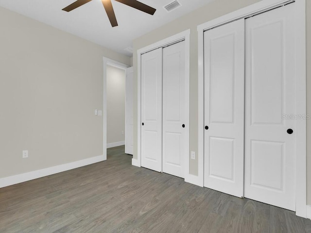 unfurnished bedroom featuring visible vents, two closets, baseboards, wood finished floors, and a ceiling fan