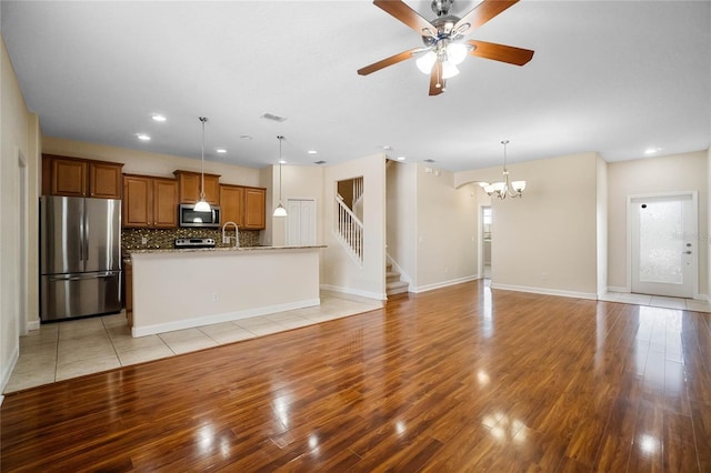 unfurnished living room with sink, ceiling fan with notable chandelier, and light hardwood / wood-style floors