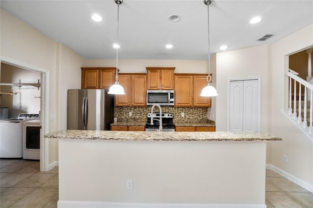 kitchen with stainless steel appliances, pendant lighting, a center island with sink, and washing machine and clothes dryer