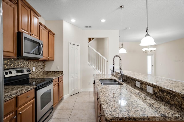 kitchen featuring sink, light stone counters, decorative light fixtures, appliances with stainless steel finishes, and a kitchen island with sink