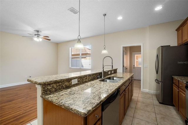 kitchen featuring sink, decorative light fixtures, an island with sink, stainless steel appliances, and light stone countertops