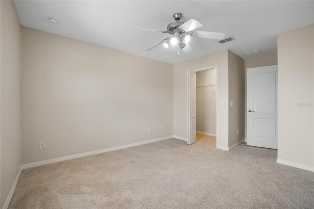 unfurnished bedroom with light carpet, a spacious closet, a closet, and ceiling fan