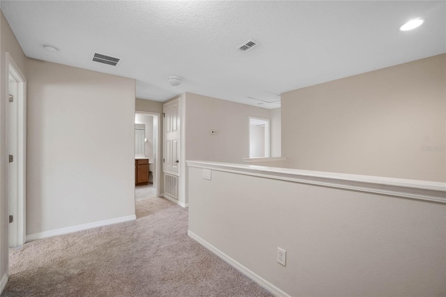 hallway with light carpet and a textured ceiling